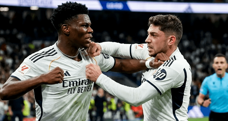 Dos futbolistas celebrando un gol en un partido, uno de ellos levantando los puños en señal de triunfo.