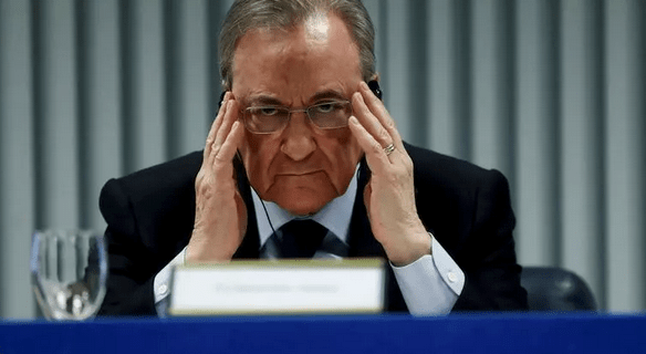 Hombre con gafas en una conferencia, frunciendo el ceño y sosteniéndose la cabeza con las manos, transmitiendo preocupación.
