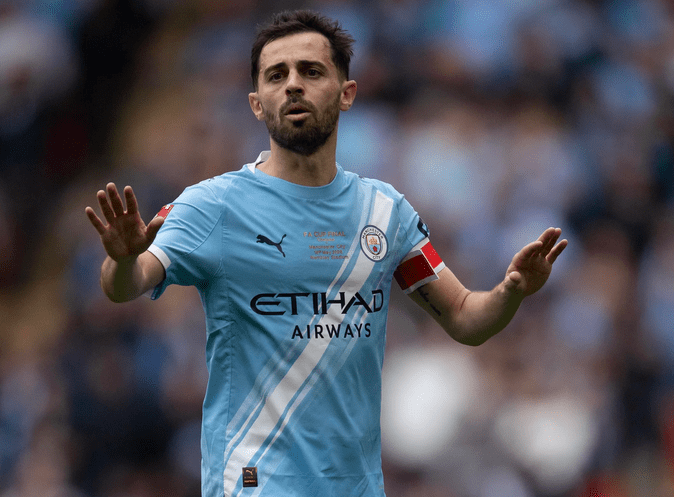 Jugador de fútbol con camiseta celeste del Manchester City, señalando con la mano mientras está en el campo.